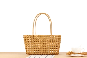 Detail view of hollow woven basket bag on a wooden table with coffee cup and flowers