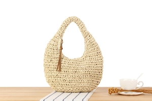 Detail of a beige woven straw handbag with a circular handle and brown leather zipper pull
