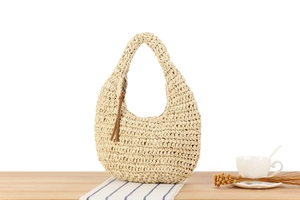 Detail of cream crochet hobo bag texture with a long brown leather tassel on wooden table