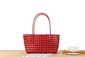 Detailed view of red hollow-out woven basket bag with slim handles on a wooden table