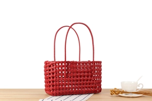 Detail of red hollow-out woven basket bag featuring dual round handles on a wooden table