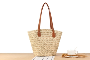 Detail shot of a large straw woven tote bag with brown leather handles on a wooden table