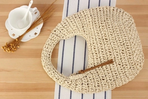 Close-up of a crescent straw handbag on a wooden table with ceramic tea set decor