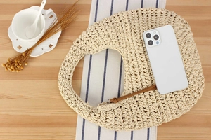 Flat lay of a beige woven half-moon hobo bag with a stylish brown leather detail strap
