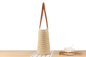 Detail of woven straw tote bag texture and brown leather straps on wooden table