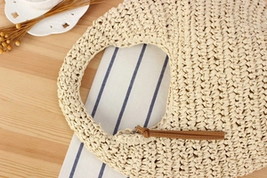 Close-up of beige woven straw bag with circular handle and brown tassel zipper detail