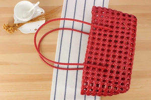 Macro detail of red woven bucket bag with hollow checkered pattern on a rustic wooden table