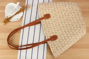 Close-up of the hand-woven straw texture and brown leather straps on a large tote bag