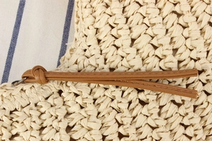 Detail of tight straw weave pattern and brown faux leather zipper pull on beach tote