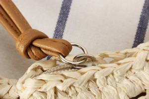 Close-up of woven straw bag detail featuring silver metal buckle and brown leather strap