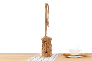 Detailed macro view of a brown hand-woven drawstring pouch with long shoulder strap