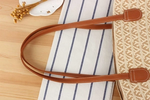 Close-up of handwoven tote bag featuring brown leather handles and decorative white stitching