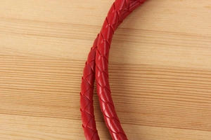 Detail of red woven leather rope strap with high-gloss finish on light wood background