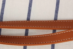 Close-up of blue and white striped canvas bag with brown leather handle and white stitching