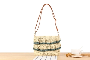 Detail of woven straw bag featuring blue-grey lace tassels and adjustable leather strap