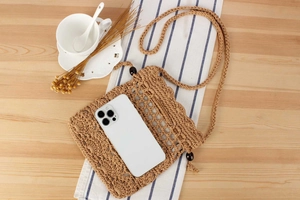 Close-up of handmade khaki crochet phone bag with wooden beads on light wood background