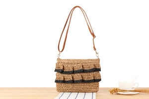 Detail of hand-woven straw bag featuring black-edged ruffles and brown faux leather strap