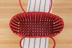 Vertical top view of bright red woven hollow-out shopping basket on wooden tabletop