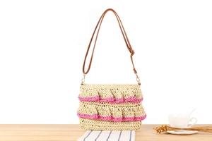 Detailed close-up of straw woven bag featuring pink ruffled trim and brown leather strap