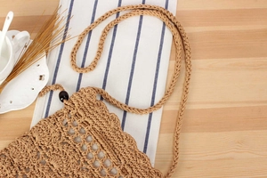 Detail of hollow woven cotton rope bag with shell closure on a rustic wooden table