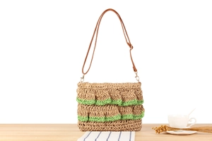 Detail of hand-woven straw bag with green crochet lace and leather strap on a wooden table
