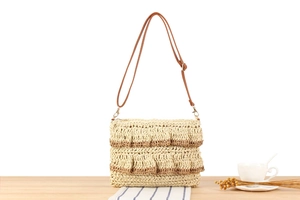 Detailed weave of a beige straw bag with brown leather strap and scalloped edges