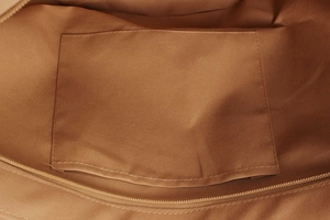 Close-up of brown woven bag interior showing fabric lining, open pocket and zipper detail