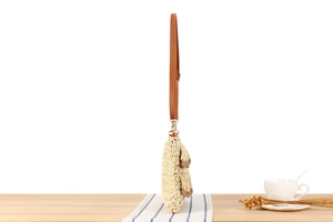 Detail view of woven straw bag side profile with brown leather strap on striped cloth