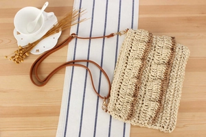 Detail of handwoven straw crossbody bag with brown leather strap and gold metal hardware