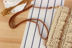 Detail of woven straw bag showing adjustable brown leather strap and gold metal buckle