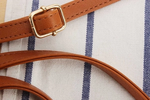 Detail of adjustable brown leather strap with polished gold buckle on a woven bag