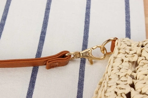Detail of woven straw bag with brown leather strap and gold lobster clasp closure