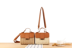 Close-up of woven straw handbag featuring brown leather handles and metal hardware detail