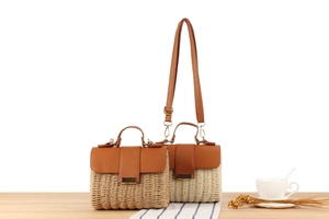 Close-up of woven straw handbag featuring brown PU leather flap and metal buckle detail