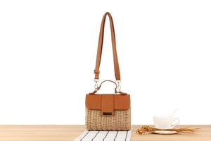 Close-up of woven crossbody bag with brown leather flap and golden handle on a table
