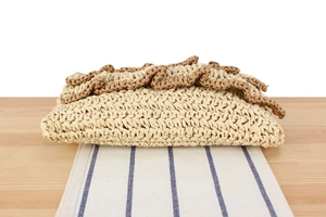 Detail of hand-woven straw bag with dark brown ruffled trim on light beige texture