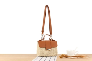 Detail of cream straw crossbody bag with brown leather flap and sleek metal clasp