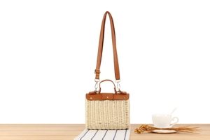 Close-up of retro woven straw crossbody bag with brown leather strap and handle detail