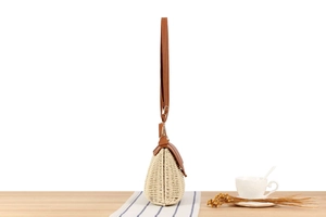 Side view of woven straw crossbody bag with brown leather flap on a stylish table setting