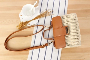 Detailed top view of woven straw crossbody bag with brown leather flap and metal clasp buckle