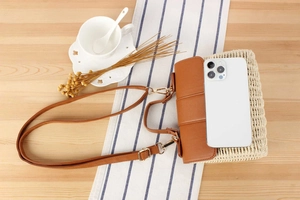 Detail of woven straw crossbody bag with leather flap shown next to a smartphone for scale