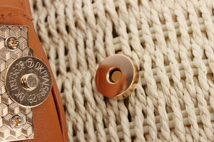 Macro shot of magnetic gold-tone metal clasp on woven bag with brown leather trim