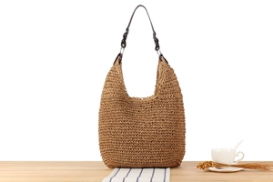 Detail of woven straw hobo bag with dark brown straps and silver metal ring accents