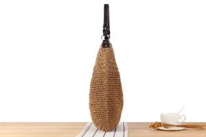 Detail showing natural raffia weave texture and black leather shoulder strap on the bag