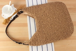Detailed weave texture of the beige straw tote bag with black leather handle on a table