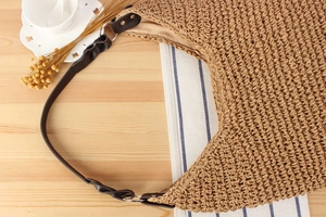 Detail of hand-woven straw hobo bag with deep brown leather shoulder strap on wood table