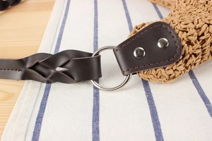 Detailed close-up of woven straw bag showing braided leather strap and metal ring