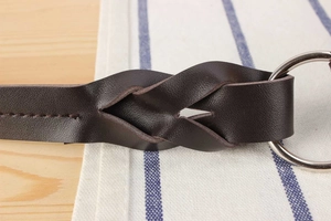 Macro detail of dark brown woven leather strap with silver metal ring and precise stitching