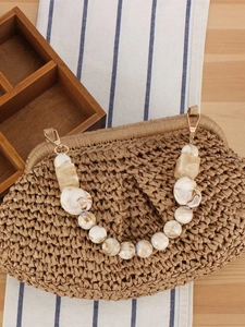 Handcrafted straw bag with marble resin chain handle and gold hardware on wooden surface