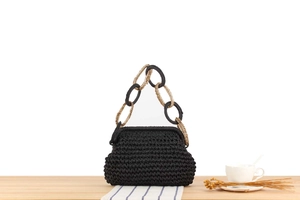 Detail of black woven straw bag with chunky gold and black chain strap for vacations
